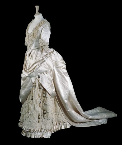 Wedding dress made by Gladman & Womack, London, 1885. Cream silk satin trimmed with embroidered net and pearl beads. Worn by May Primrose to marry Major Herbert Littledale on 10 June 1885 in Cheltenham. Given by the Hon.S.F. Tyser