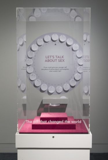Display case with one contraceptive pill stating 'the pill that changed the world' against a backdrop of visitors' comments 'Let's talk about sex'
