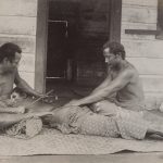 Two Samoan men tattoo a man lying on the floor