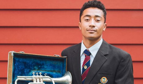Young Tongan man stands in his school uniform holding a trumpet
