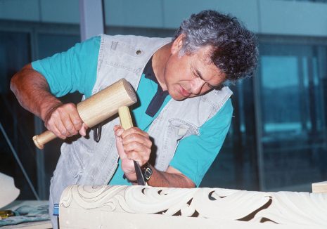 A man is carving a piece of wood with an adze.