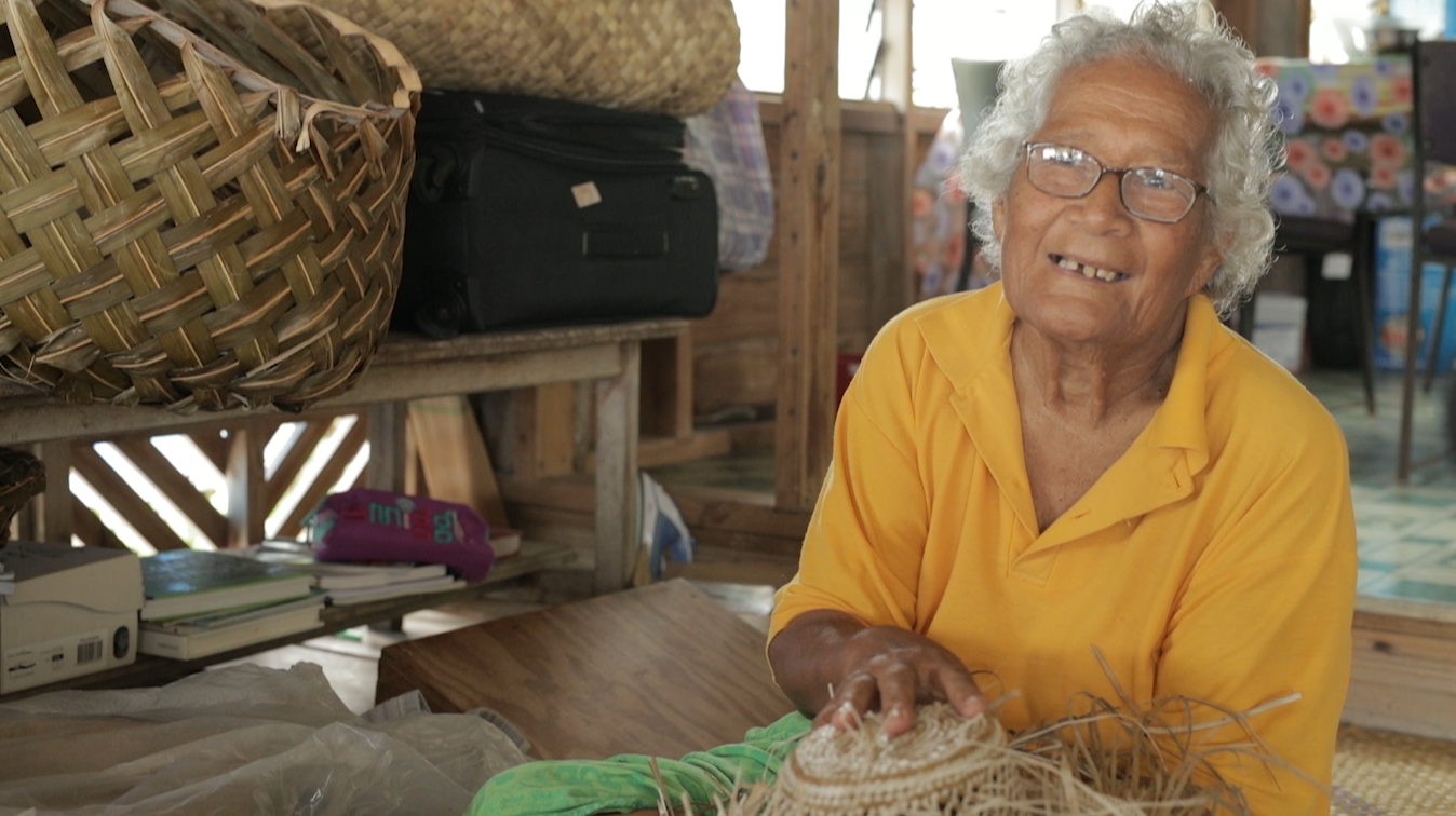 A lady in a yellow shirt holds up some of her weaving