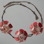 A necklace made by Colin McCahon. It features three handcrafted red flowers on a thin woven rop