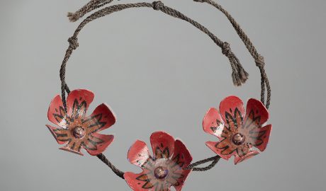 A necklace made by Colin McCahon. It features three handcrafted red flowers on a thin woven rop