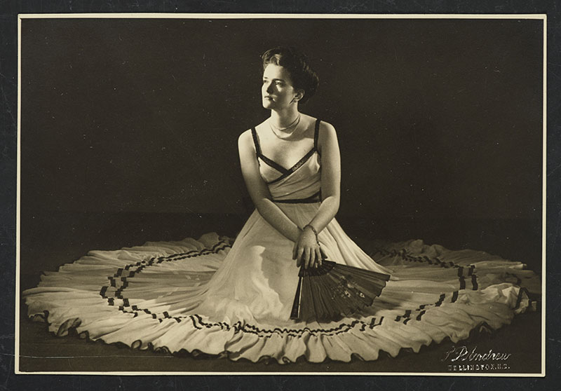 Sepia image of a woman sitting in the middle of a large white dress holding a fan