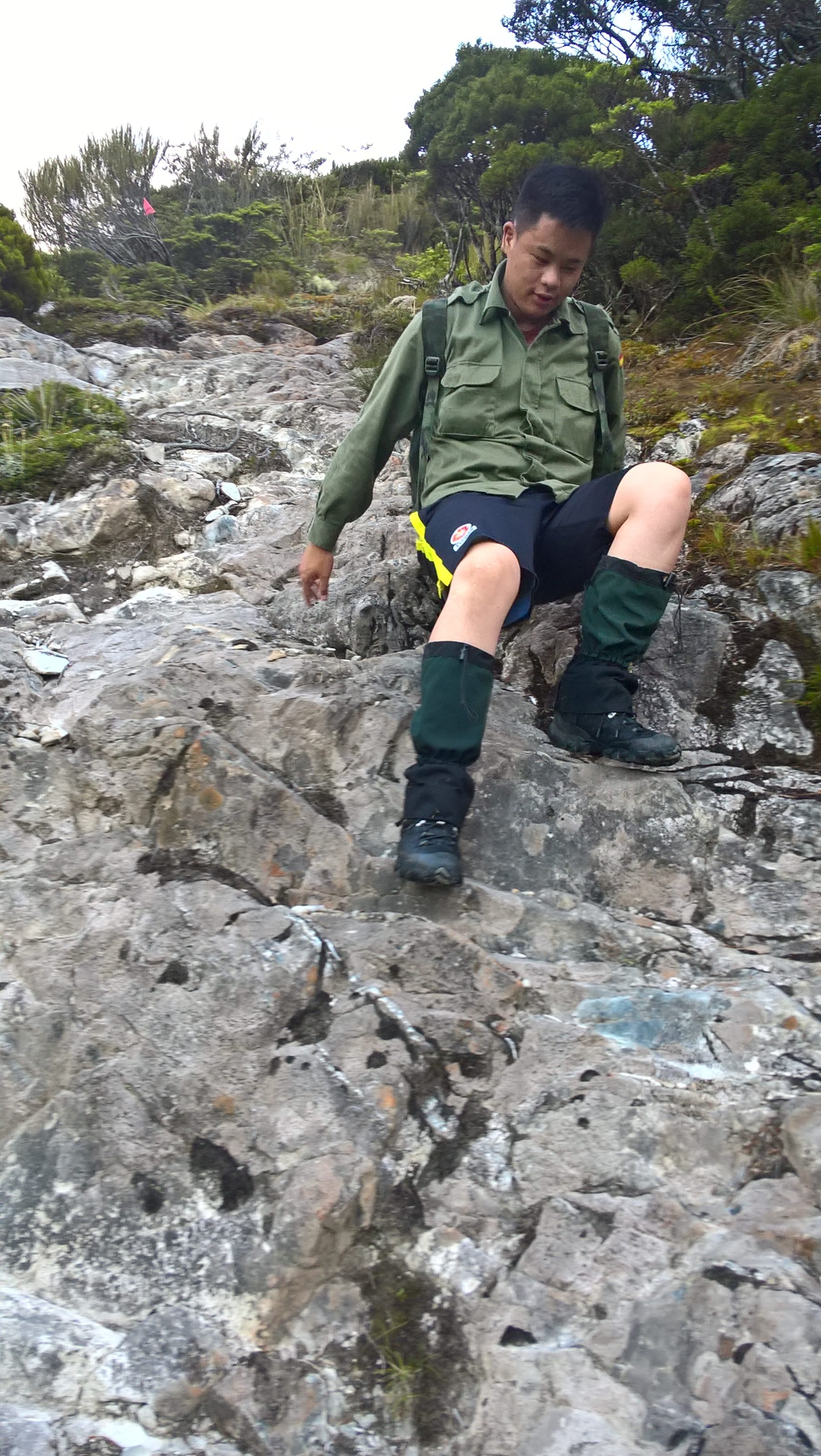 A man shuffling down the side of a rocky piece of land on a mountain. 