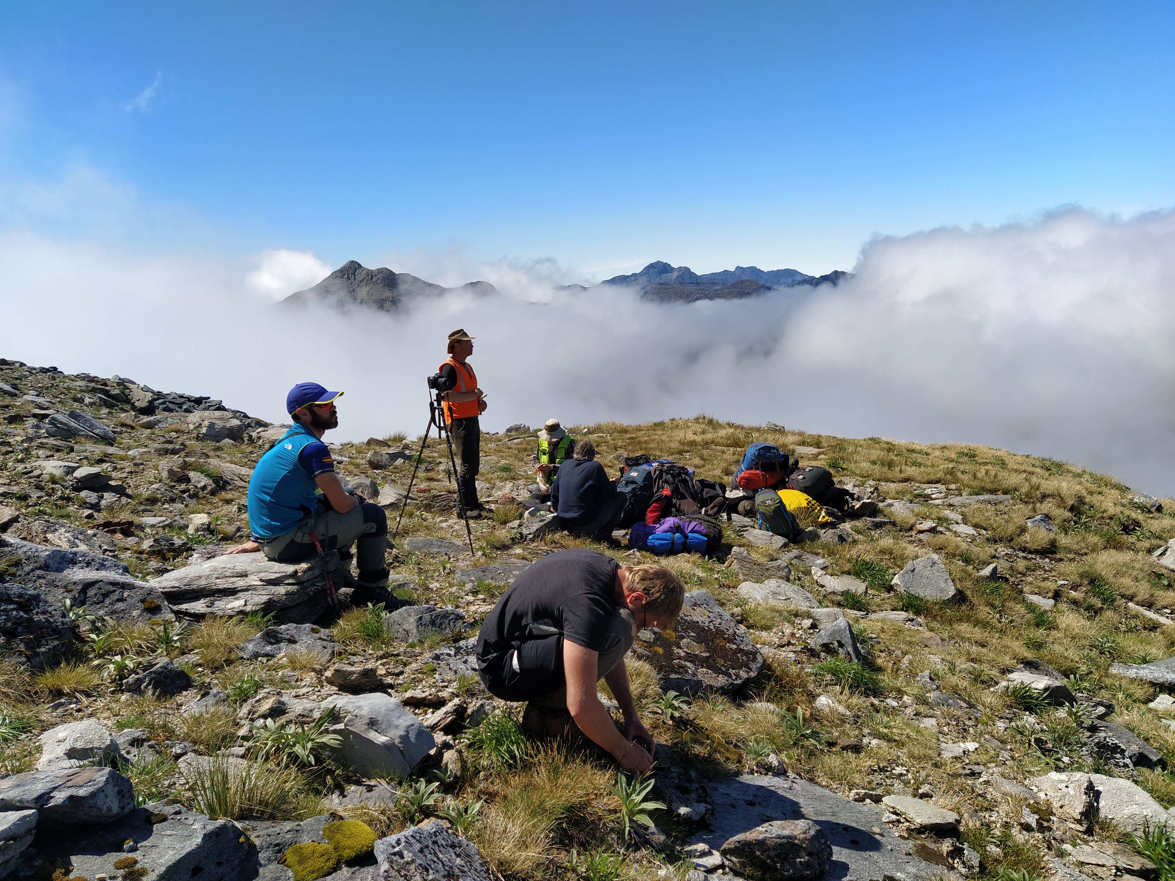 Four people on top of a mountain surrounded by camping gear and low clouds in the background