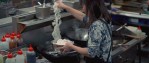 A woman adds noodles to a bowl on a stove in a restaurant kitchen