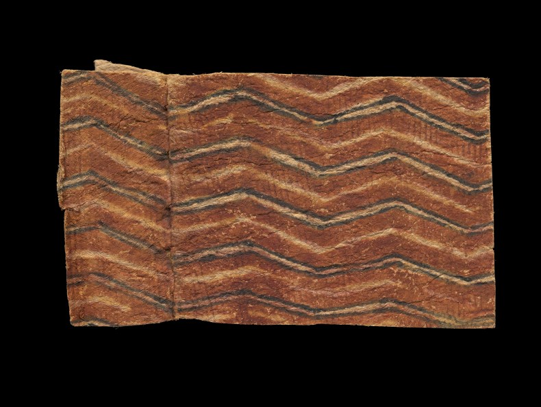 A piece of tapa cloth with brown, black, and cream lines painted on it. It's sitting on a black background.
