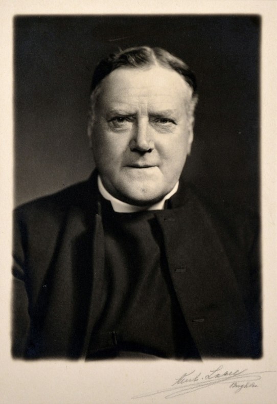 A black and white head and shoulders photograph of a priest 
