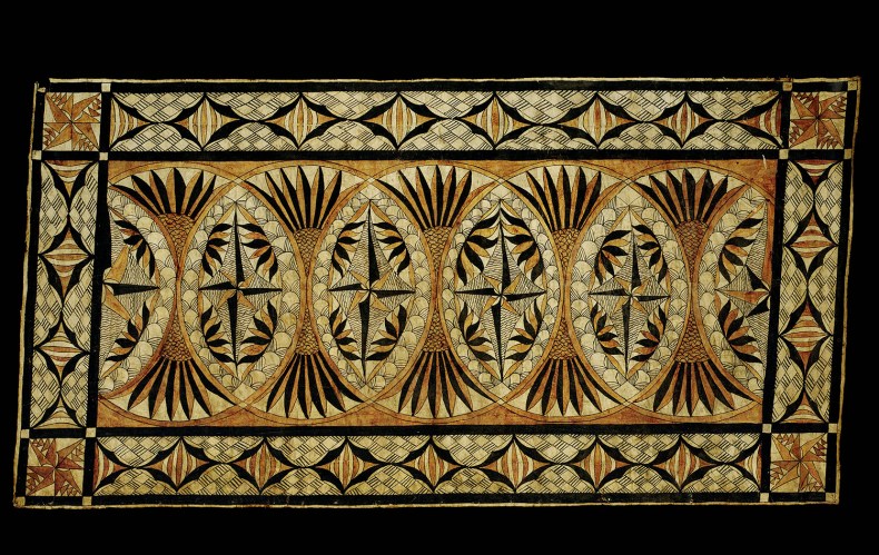 An intricately patterened piece of tapa cloth with lots of shapes in different shades of brown and black, sitting on a black background
