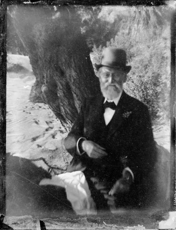 A black and white photograph of a man in a rounded top hat and a suit sitting on a horse