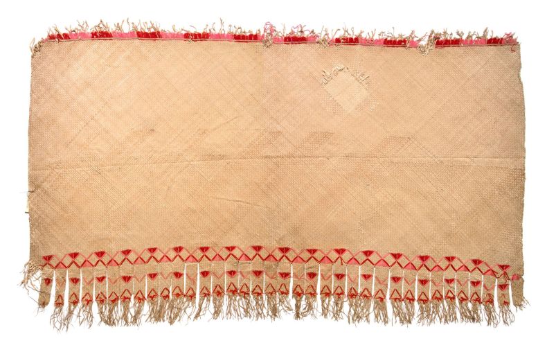 A large woven mat with red trim at the top and red zig-zag patterns at the bottom with long tassles.