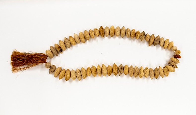 A natural-coloured karaka berry necklace with a muka, or flax string tassle at one end.