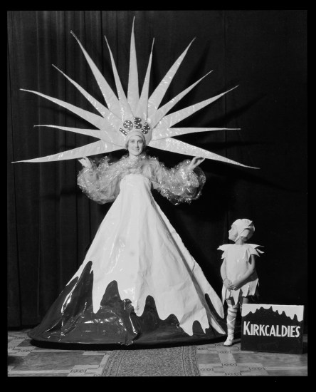 A black and white photo of a woman in a costume dressed as a mountain with snow on it and a pointy star headdress